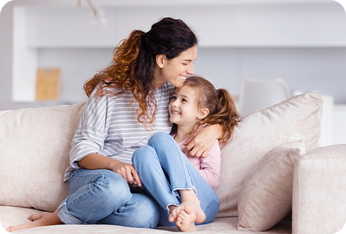 Mãe e filha se abrançando sentadas no sofá em uma sala de estar.